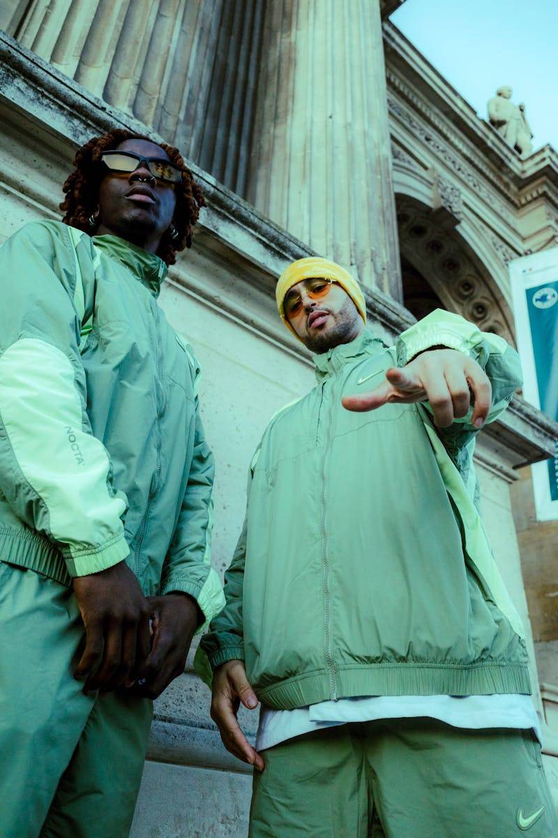Two young men in green streetwear posing with confidence by an architectural column.