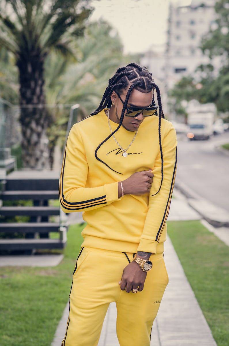 Fashionable man with dreads in bright yellow outfit posing outdoors.