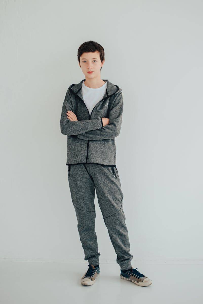 Teenage boy posing with crossed arms in a gray tracksuit against a white background.