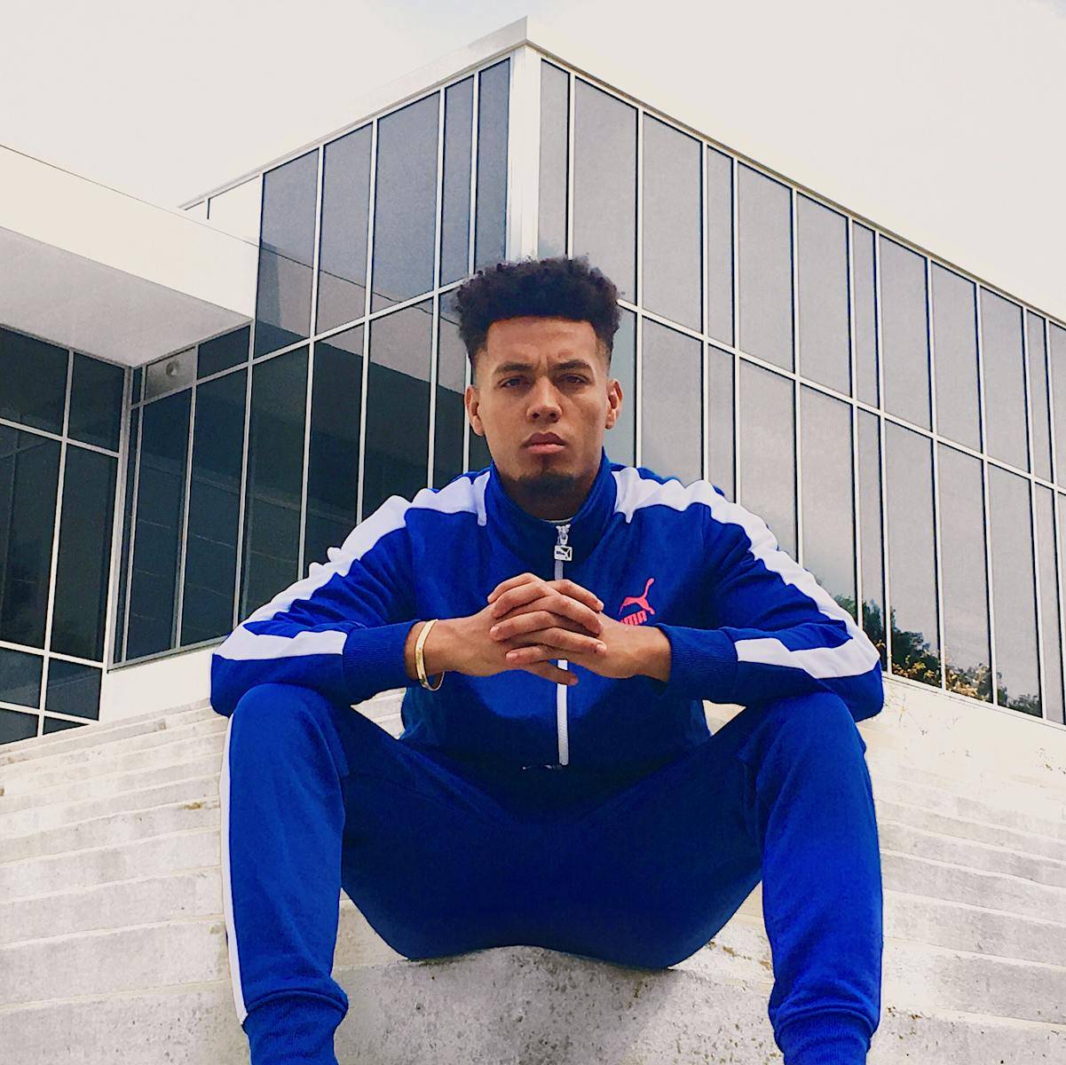 Serious man in blue sportswear sitting on steps with modern building backdrop.
