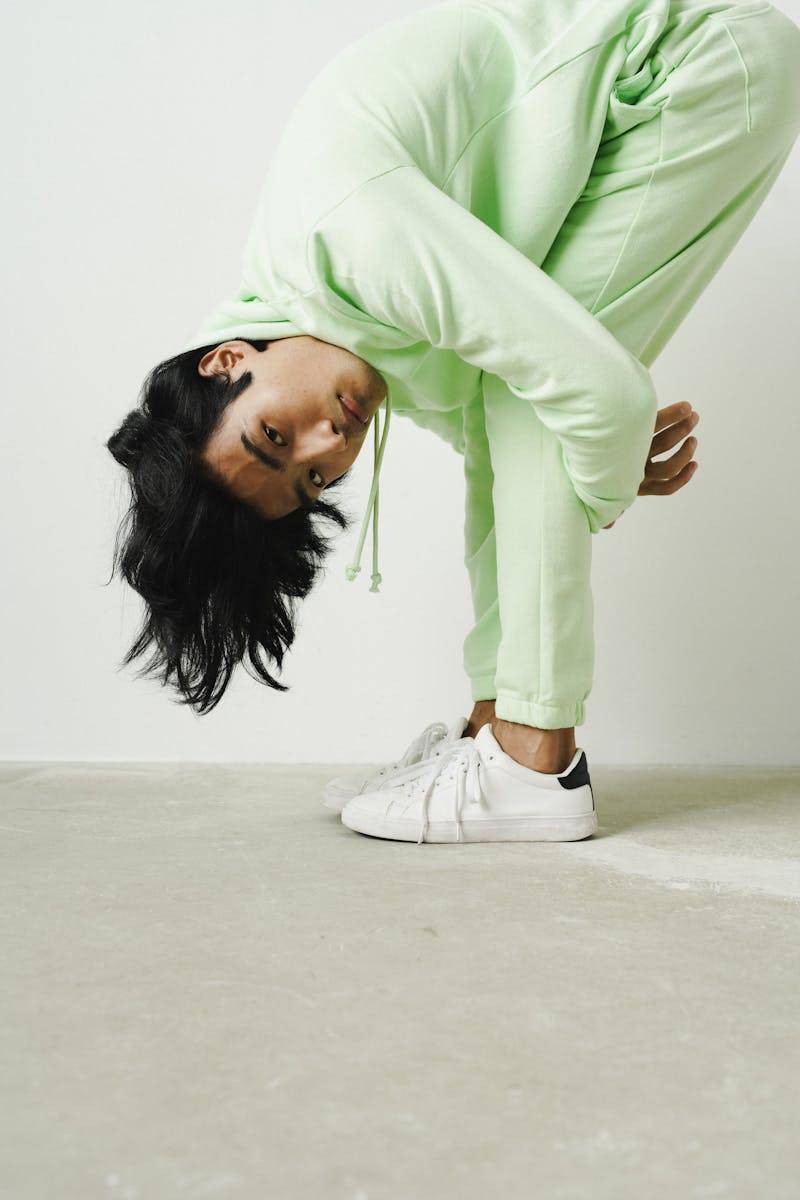 Man in light green tracksuit strikes a unique pose in a minimalist studio.